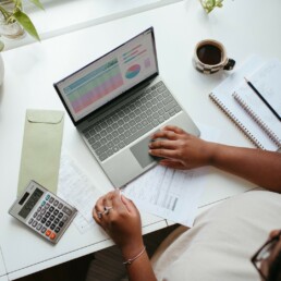 Someone working at a desk with a laptop, calculator, & paperwork.