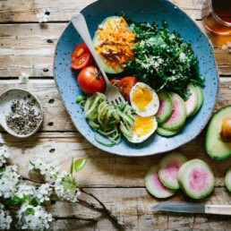 A dinner plate on a wooden table filled with health food including tomatoes & greens.